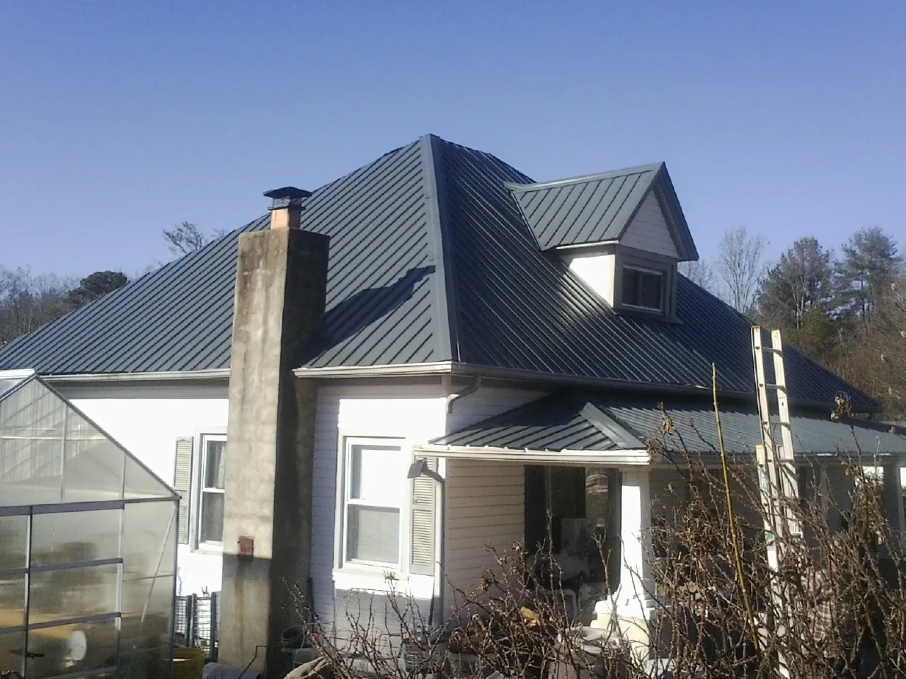 Dark blue standing seam metal roof on a white farmhouse with dormer — Slate & Tile Roof Repair by Roofing Brothers in Fisherville