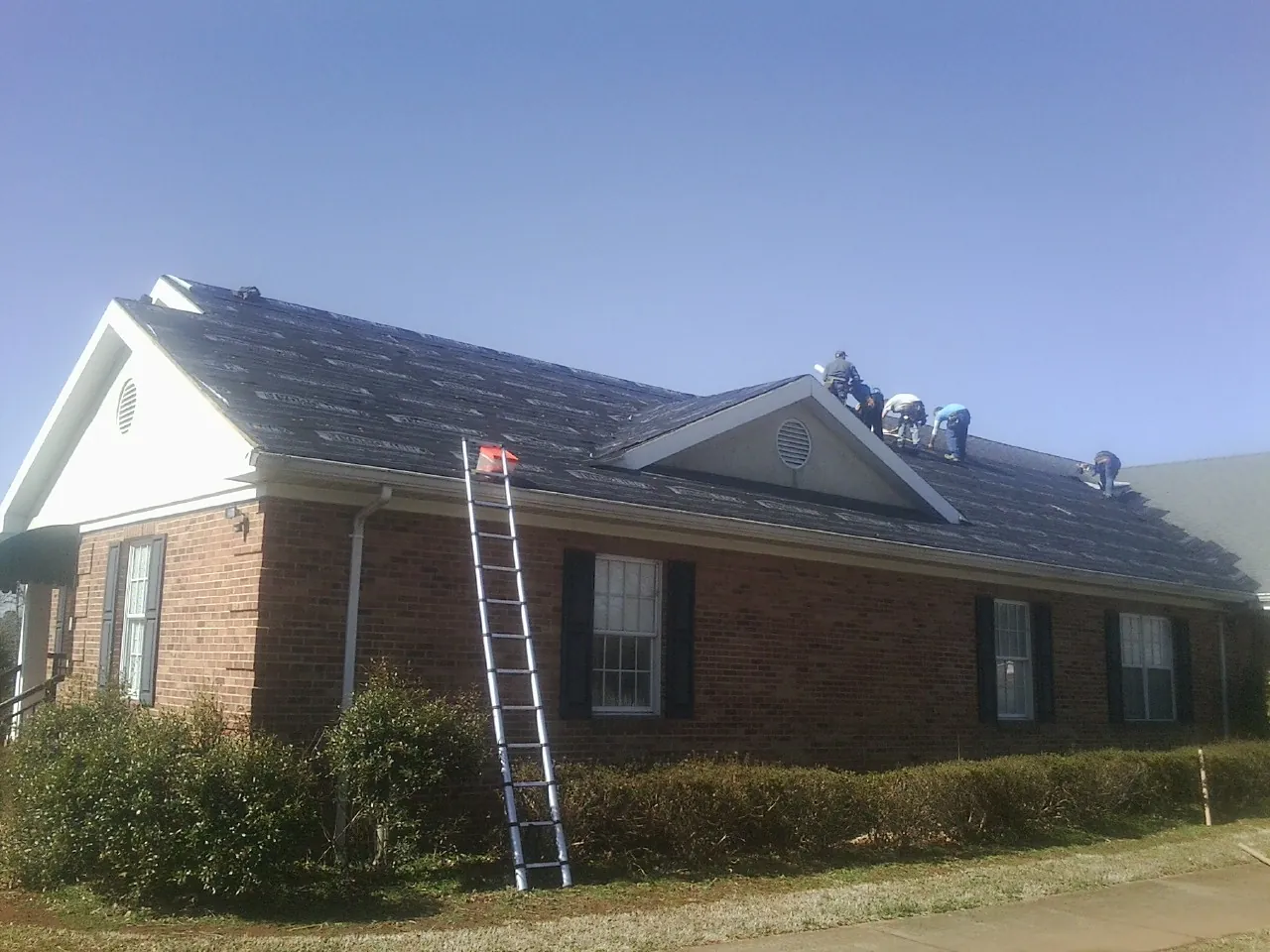 Crew tearing shingles off a brick ranch roof with a ladder set — Metal Roof Repair work by our crew in Fisherville