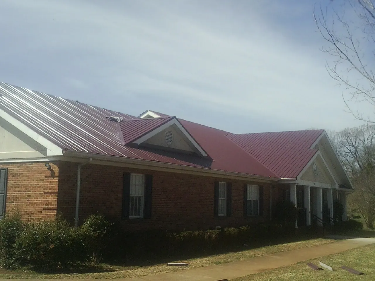 Red metal roof with gabled entries on a long brick building, from a Hail Damage Roof Repair job in Fisherville