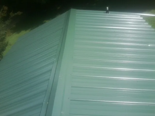 New green metal panels meeting at the ridge of a roof — Flat Roof Repair work by our crew in Fisherville