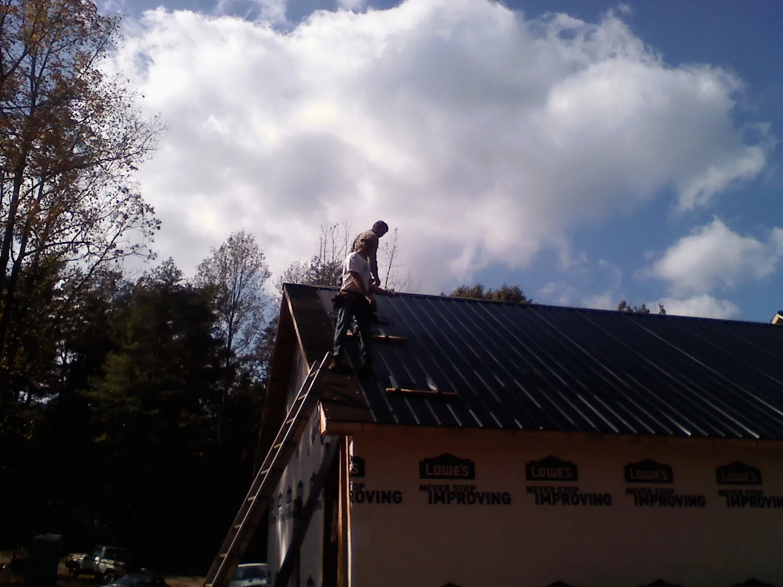 Roofer fastening dark metal panels high against a cloudy sky, from a Roof Inspection job in Fisherville