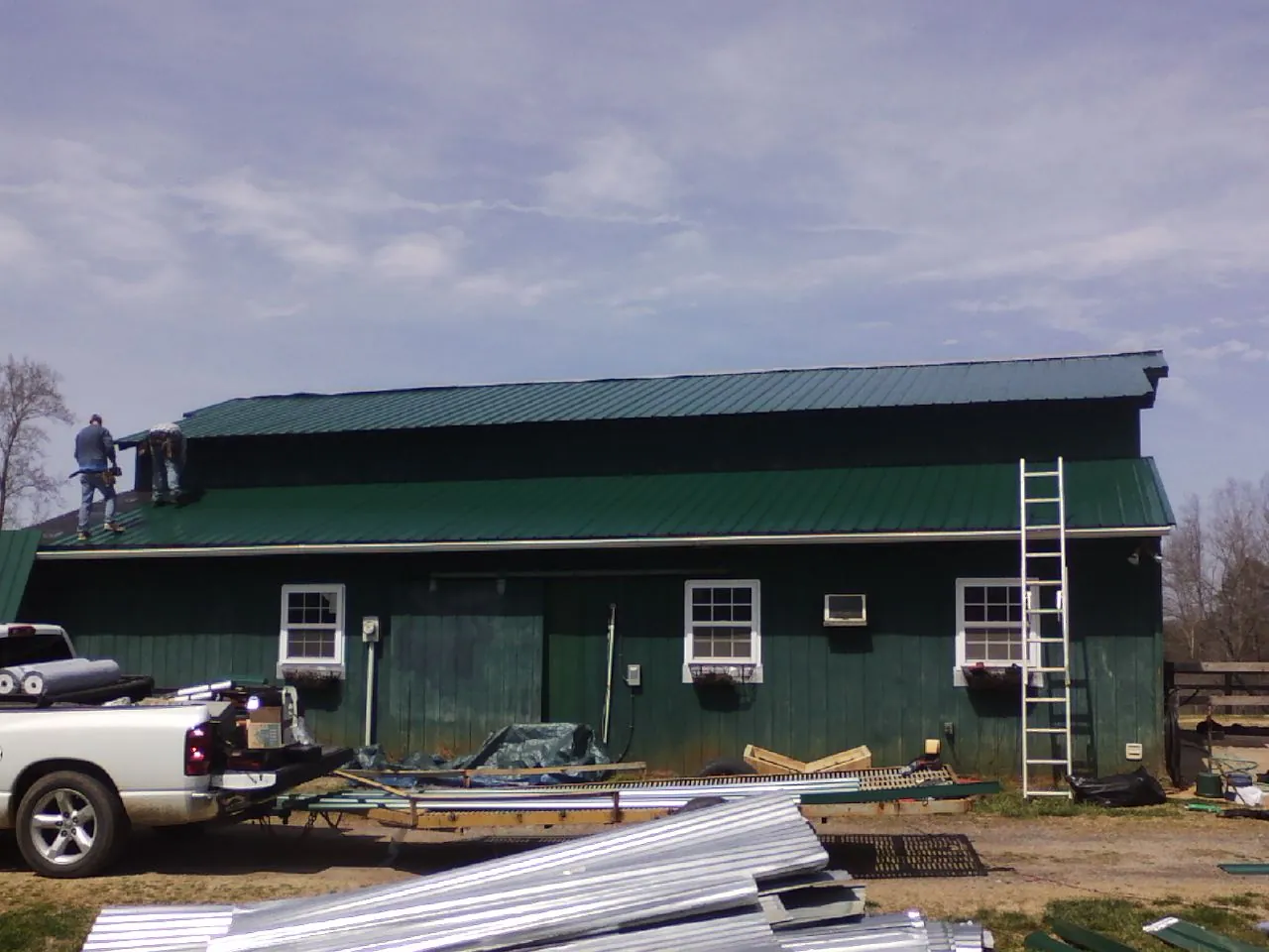 Crew installing green metal roofing on a large green barn in Fisherville
