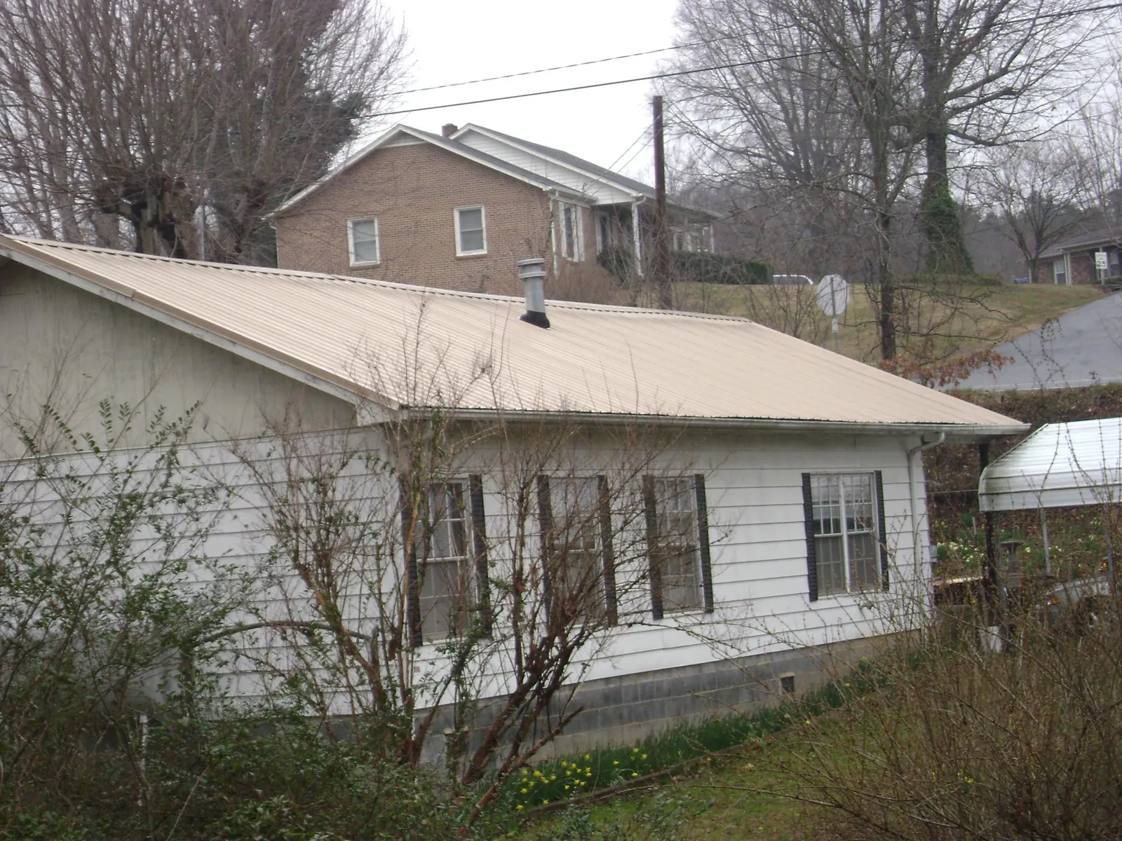 Tan metal roof on a white sided house set into a hillside — Commercial Roofing by Roofing Brothers in Fisherville