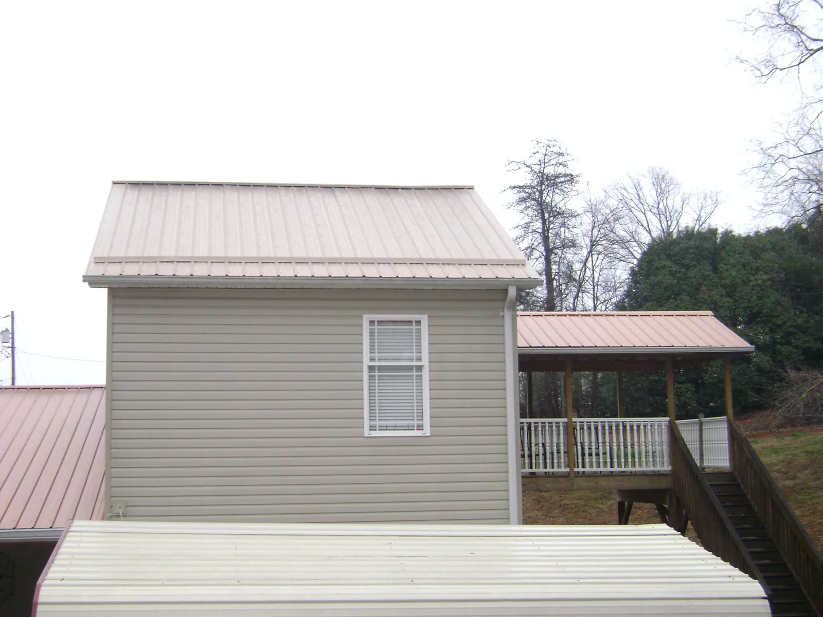 Tan metal roofs on a two story addition and attached porch, from a Roof Replacement job in Fisherville